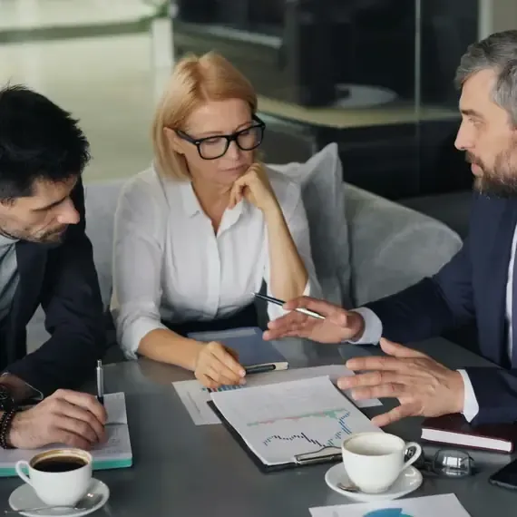 Three business professionals discussing printed charts at a table